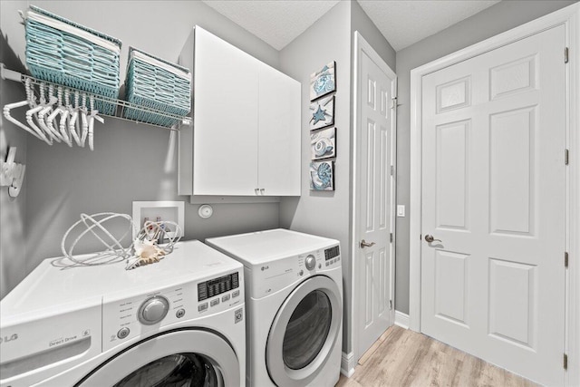 laundry area featuring washer and clothes dryer, light wood-type flooring, a textured ceiling, and cabinets