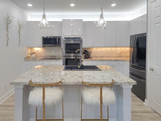 kitchen with black appliances, an island with sink, white cabinetry, and pendant lighting