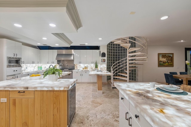 kitchen with light stone counters, wall chimney exhaust hood, white cabinets, a kitchen island, and stainless steel microwave