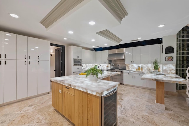 kitchen with appliances with stainless steel finishes, light stone counters, wall chimney exhaust hood, white cabinetry, and a kitchen island