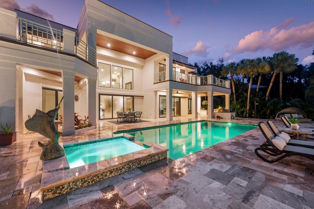 pool at dusk featuring an in ground hot tub and a patio area