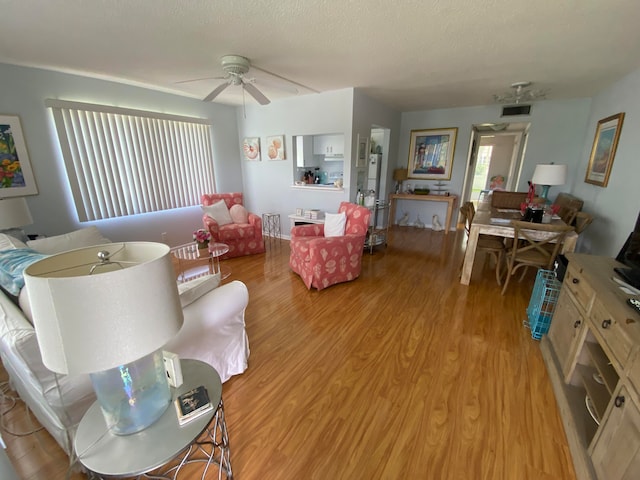 living room featuring ceiling fan, light hardwood / wood-style floors, and a textured ceiling