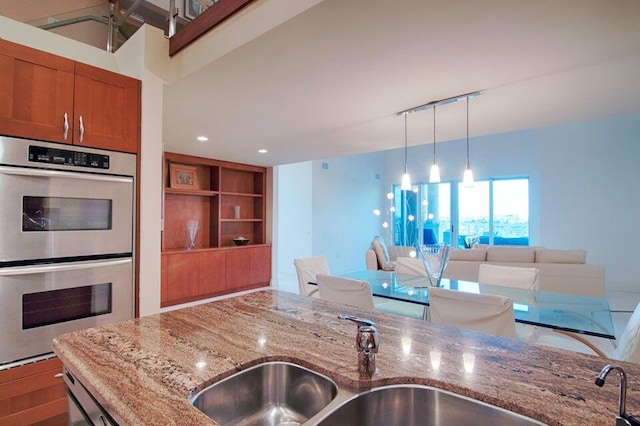 kitchen featuring decorative light fixtures, stainless steel double oven, light stone countertops, and sink