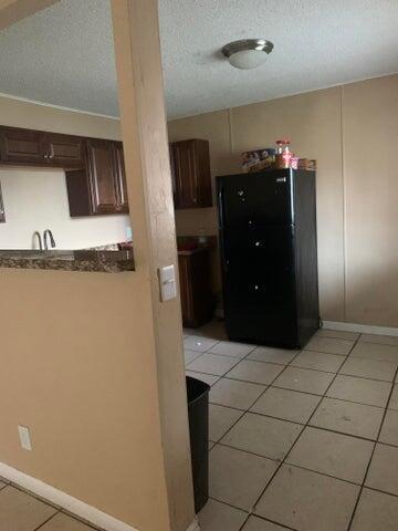 kitchen with a textured ceiling, light tile flooring, dark brown cabinets, and black refrigerator