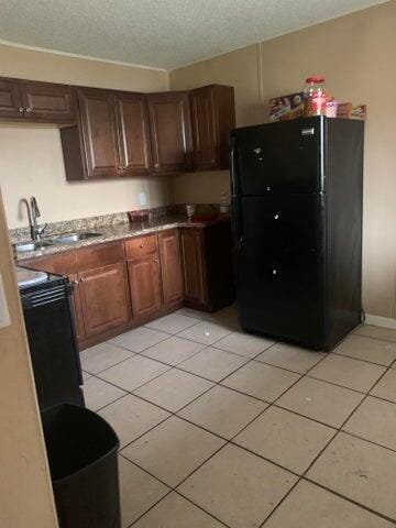 kitchen with black refrigerator, sink, a textured ceiling, and light tile floors