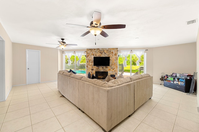 living room featuring a stone fireplace, a wealth of natural light, ceiling fan, and light tile floors