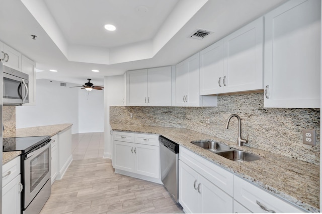 kitchen with light stone countertops, appliances with stainless steel finishes, white cabinetry, sink, and a tray ceiling