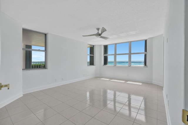 tiled empty room featuring a water view, ceiling fan, and a textured ceiling