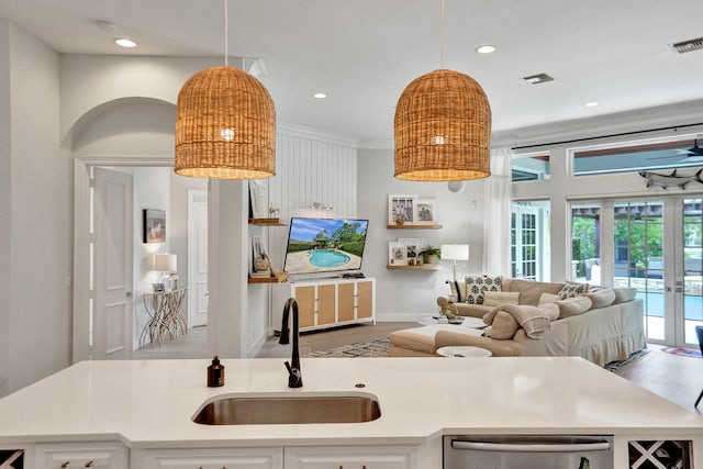 kitchen with a kitchen island with sink, french doors, white cabinets, sink, and decorative light fixtures