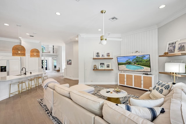 living room featuring ceiling fan, crown molding, light hardwood / wood-style flooring, and sink