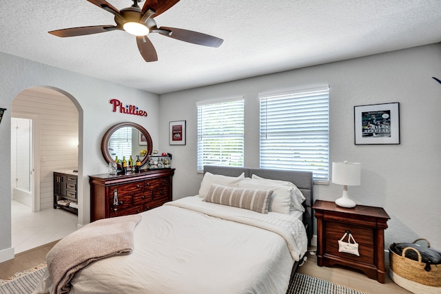 bedroom featuring a textured ceiling, ceiling fan, connected bathroom, and light hardwood / wood-style flooring