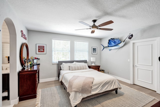 bedroom featuring ceiling fan, a textured ceiling, connected bathroom, and light hardwood / wood-style floors