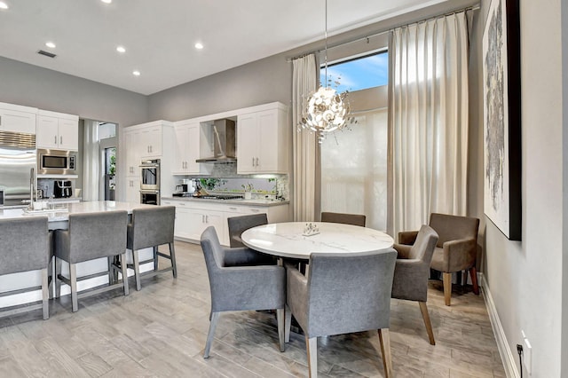 dining area with sink, light wood-type flooring, and an inviting chandelier