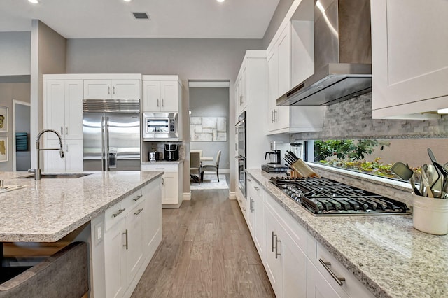 kitchen featuring light hardwood / wood-style floors, tasteful backsplash, built in appliances, wall chimney exhaust hood, and sink