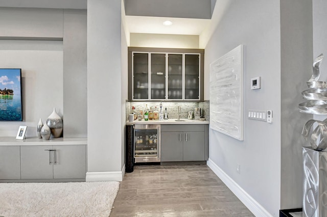 bar featuring wine cooler, gray cabinetry, light hardwood / wood-style floors, and tasteful backsplash