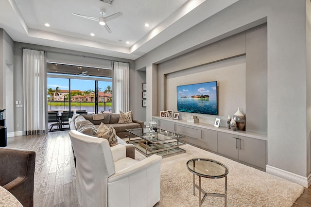 living room featuring ceiling fan, light hardwood / wood-style floors, and a tray ceiling