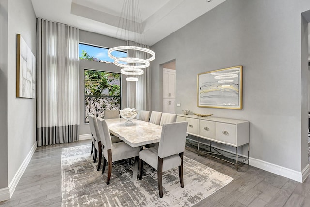 dining area with a chandelier, a raised ceiling, and light hardwood / wood-style flooring