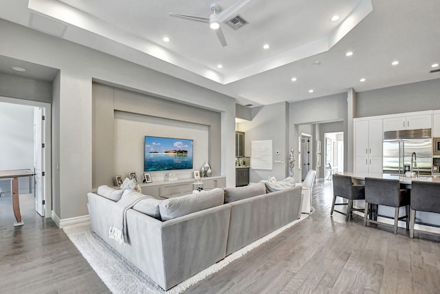 living room with ceiling fan, a raised ceiling, light hardwood / wood-style flooring, and sink