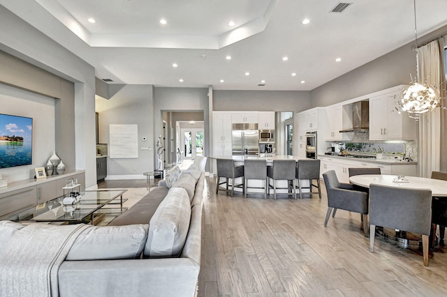 living room featuring a tray ceiling, light wood-type flooring, and a chandelier