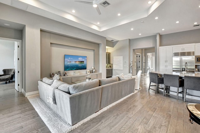 living room featuring sink, ceiling fan, light hardwood / wood-style floors, and a tray ceiling