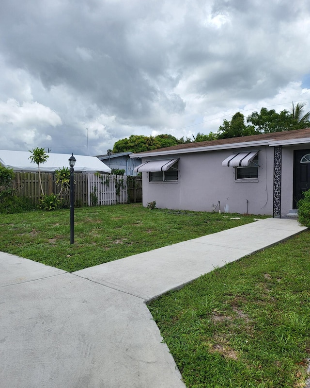 view of side of home with a lawn, fence, and stucco siding