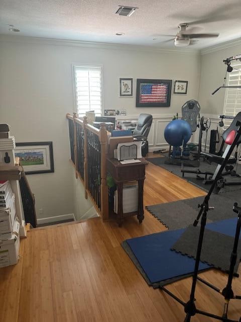 exercise area with crown molding, a textured ceiling, light wood-type flooring, and ceiling fan