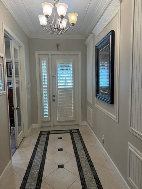 doorway to outside with a notable chandelier, light tile floors, and crown molding