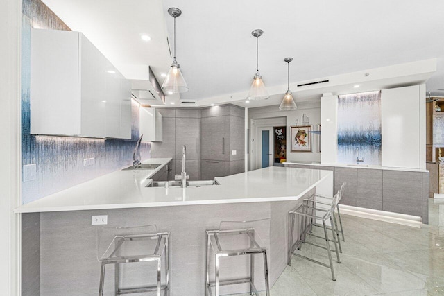 kitchen featuring decorative light fixtures, sink, white cabinets, a kitchen breakfast bar, and kitchen peninsula