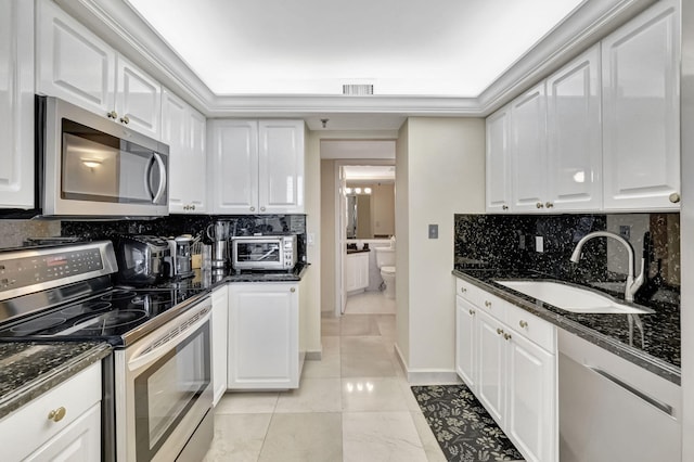 kitchen featuring white cabinetry, sink, backsplash, dark stone counters, and appliances with stainless steel finishes