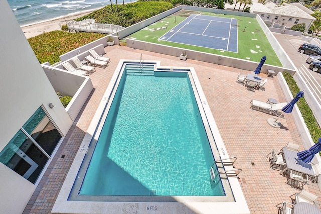 view of swimming pool featuring a water view, a view of the beach, tennis court, and a patio