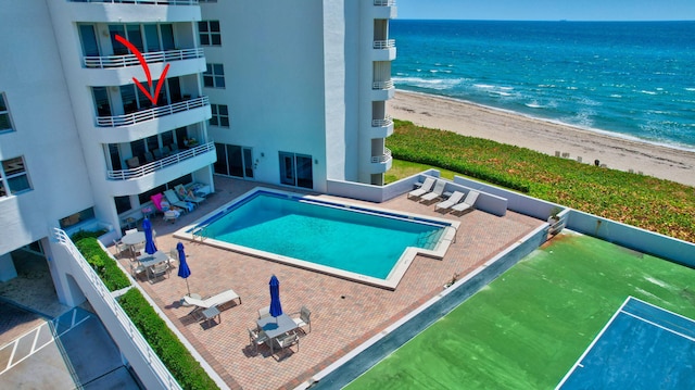 view of swimming pool with a water view, a beach view, and a patio