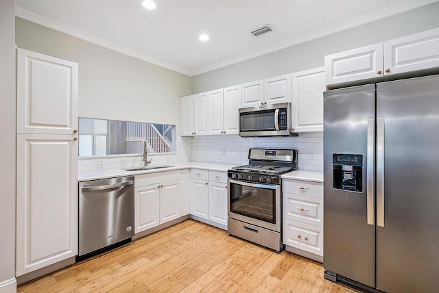 kitchen with white cabinetry, stainless steel appliances, decorative backsplash, sink, and ornamental molding