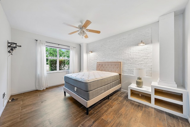 bedroom featuring ceiling fan, brick wall, dark hardwood / wood-style flooring, and decorative columns