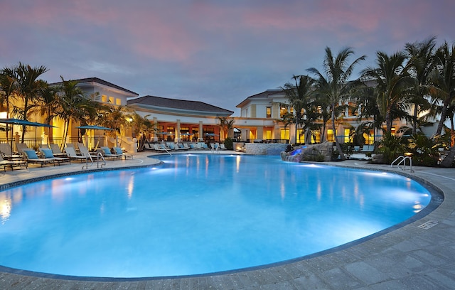 pool at dusk featuring pool water feature and a patio