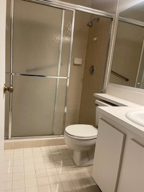 bathroom with tile patterned floors, vanity, a shower with shower door, and toilet