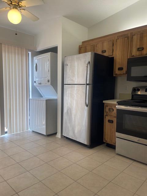 kitchen featuring light tile patterned floors, stainless steel appliances, ceiling fan, and stacked washer and clothes dryer