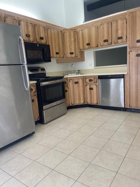 kitchen featuring a towering ceiling, appliances with stainless steel finishes, sink, and light tile patterned flooring