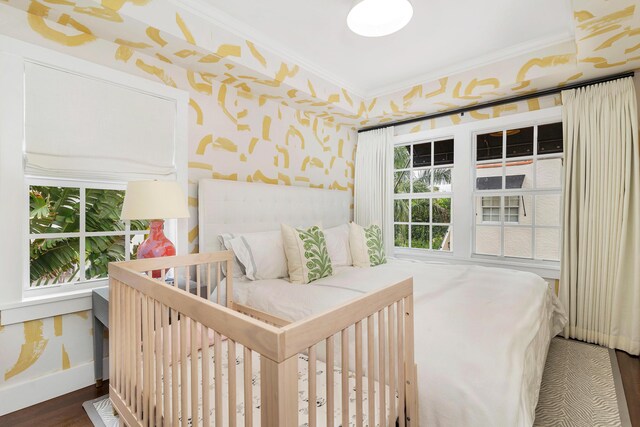 bedroom featuring a crib, dark hardwood / wood-style flooring, and ornamental molding