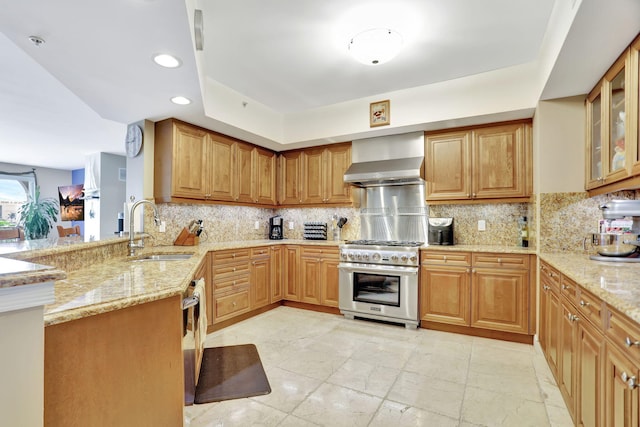 kitchen with light stone countertops, sink, wall chimney exhaust hood, stainless steel appliances, and kitchen peninsula