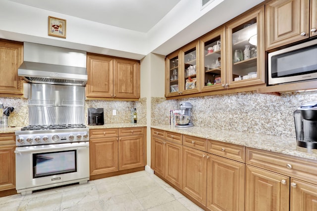 kitchen with light stone countertops, wall chimney exhaust hood, appliances with stainless steel finishes, and tasteful backsplash