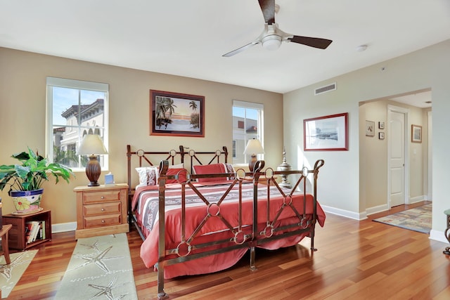 bedroom with ceiling fan, wood finished floors, visible vents, and baseboards