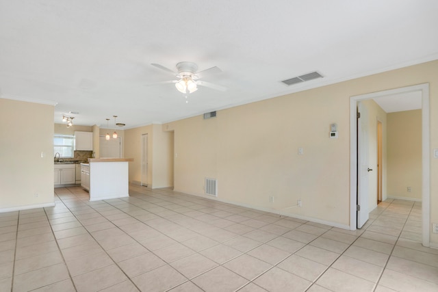 unfurnished living room with ceiling fan, sink, light tile patterned flooring, and ornamental molding