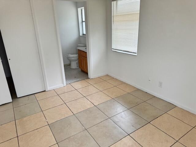 unfurnished bedroom with ensuite bathroom and light tile floors