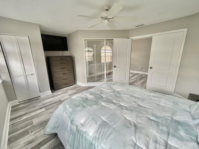 bedroom featuring a textured ceiling, two closets, light hardwood / wood-style flooring, and ceiling fan