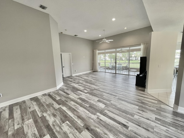 unfurnished living room featuring ceiling fan, a towering ceiling, a textured ceiling, and light hardwood / wood-style flooring