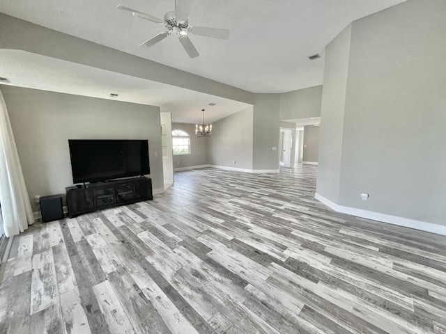 unfurnished living room featuring ceiling fan with notable chandelier and light wood-type flooring