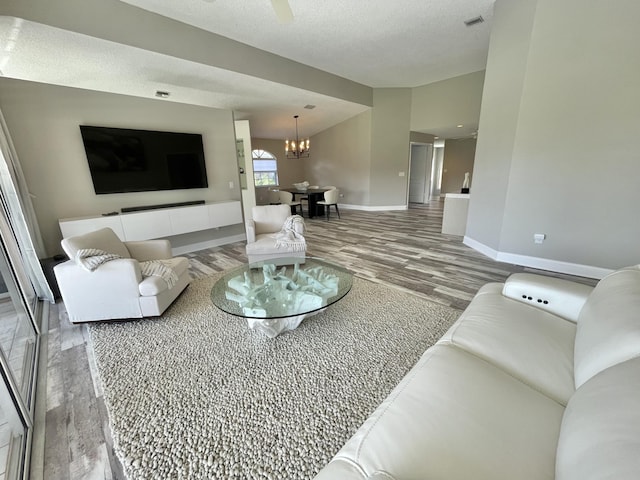 living room with ceiling fan with notable chandelier, wood-type flooring, and a textured ceiling