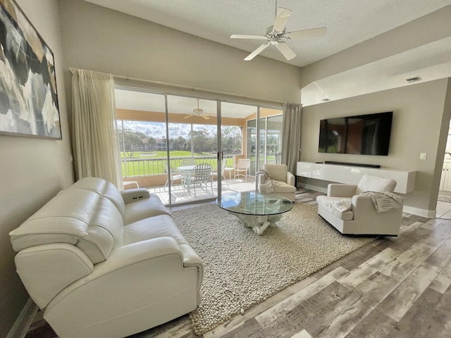 living room featuring ceiling fan, light hardwood / wood-style flooring, and a textured ceiling