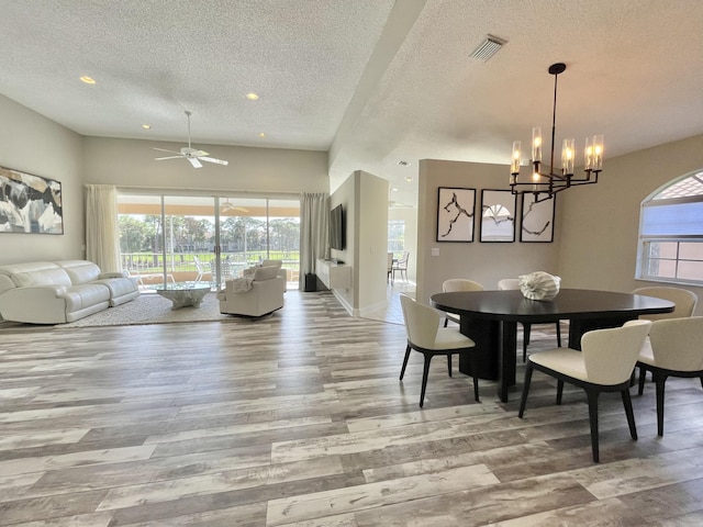 dining space with ceiling fan with notable chandelier, a textured ceiling, and light hardwood / wood-style flooring