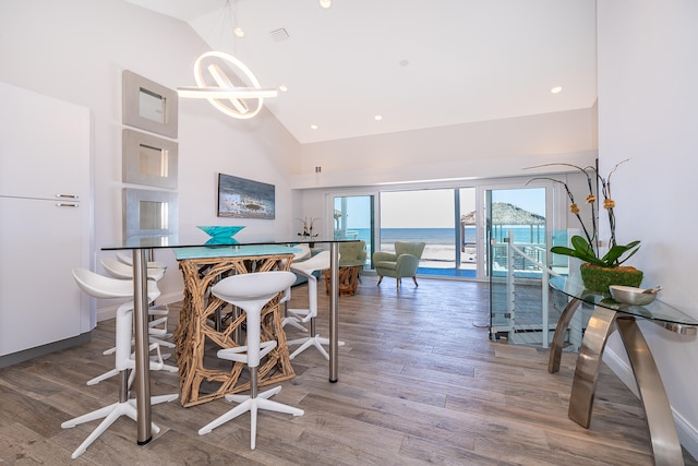 dining area with high vaulted ceiling, wood-type flooring, and a water view